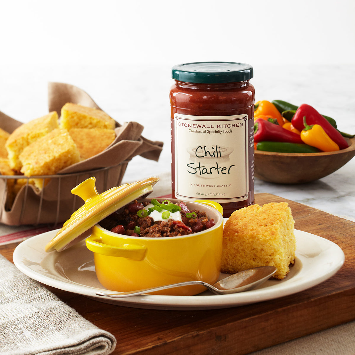 chili in a yellow crock with cornbread in a basket and a jar of Stonewall Kitchen Chili Starter