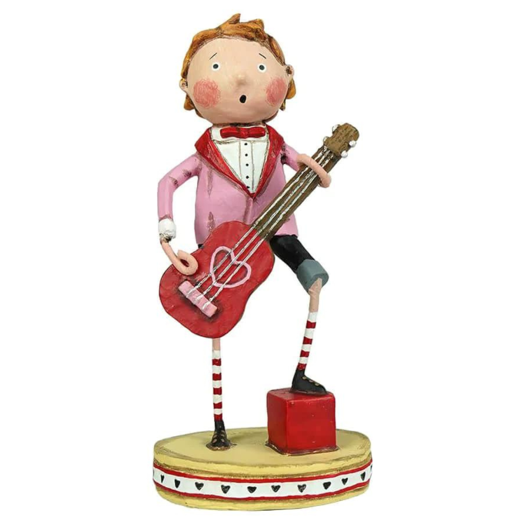 A whimsical figurine of a boy playing a red guitar, designed by Lori Mitchell. He wears a pink jacket, red bow tie, and mismatched striped socks, standing on a yellow base decorated with hearts.