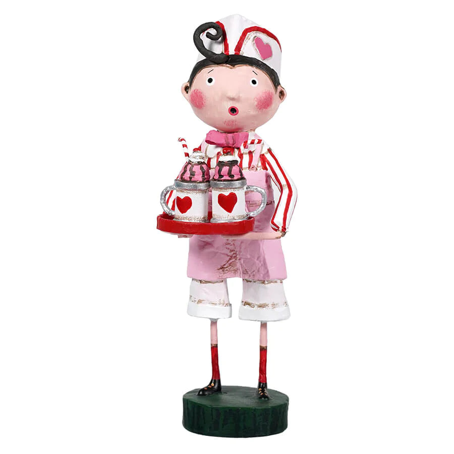 A whimsical figurine of an ice cream scooper with a pink apron and red and white striped shirt, holding two cups of ice cream. The figurine has a playful facial expression and is standing on a green base.