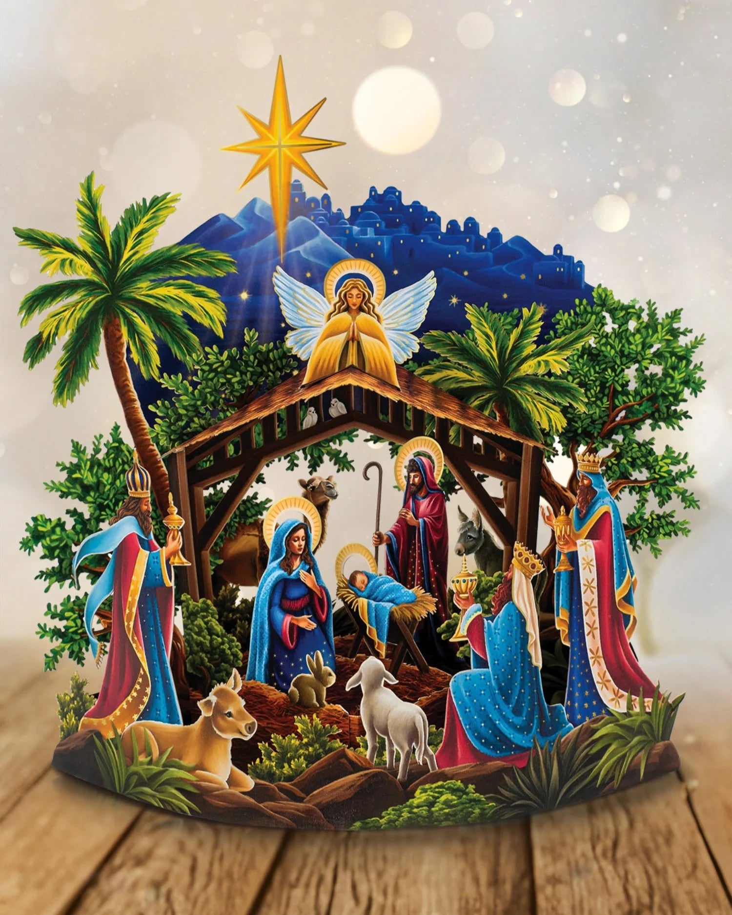 Product photo showing a three dimensional manger scene depicting the Nativity and the birth of the baby Jesus, with the three kings bearing gifts and surrounded by animals from the manger. An angel is shown looking down from above and a large star rises over the town of Bethlehem depicted in the background of the image