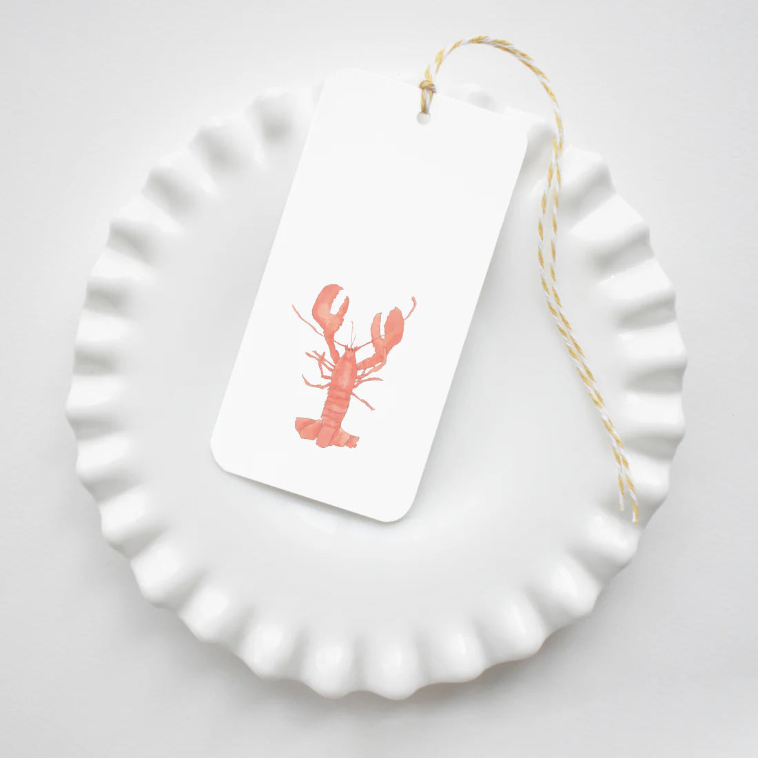 White plate showing a Sara Fitz Gift Tag with a red lobster design on a white background
