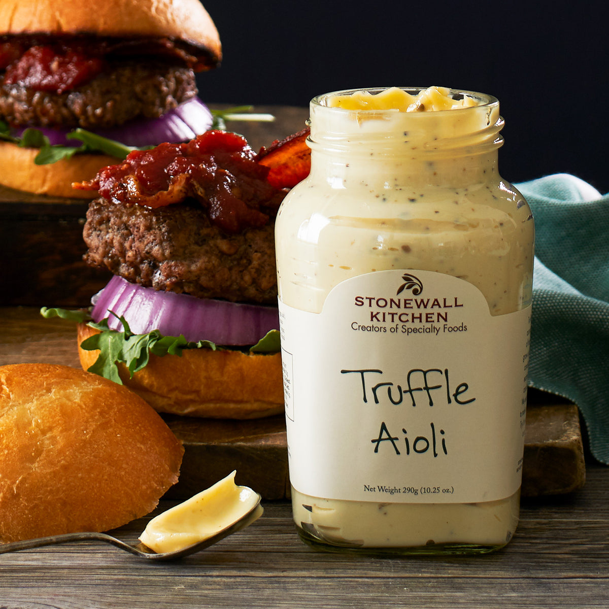 jar of Stonewall Kitchen Truffle Aioli in front of hamburgers with bacon, lettuce, and red onion
